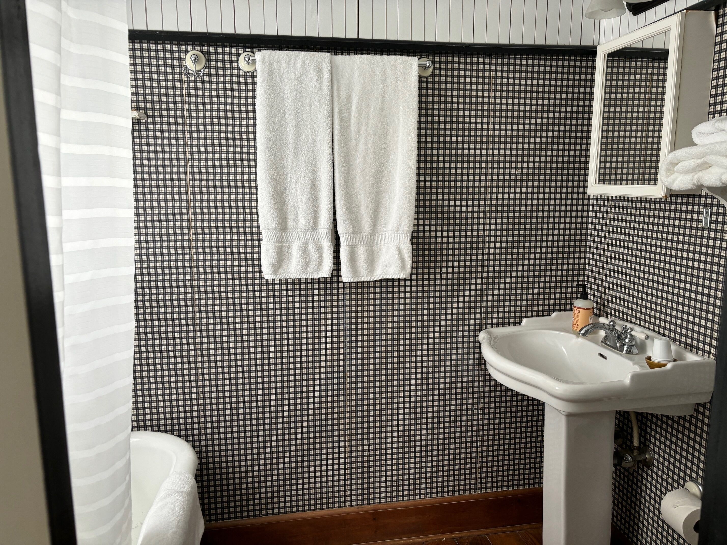 A bathroom with a checkered black and white tiled wall, a white sink with a mirror above it, and a white bathtub.