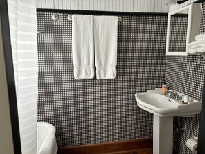A bathroom with a checkered black and white tiled wall, a white sink with a mirror above it, and a white bathtub. - Folkestone Inn (Bryson City)