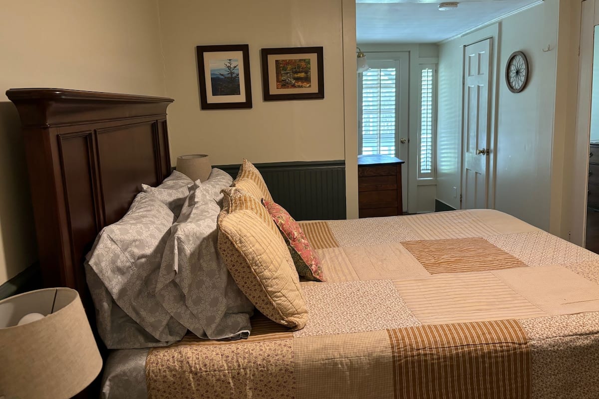 A bedroom with a bed, a dresser, and a door leading to another room.