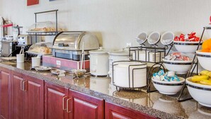 A buffet setup with various food items and condiments, including a coffee machine, a food warmer, and several bowls containing fruits and snacks. - Comfort Inn Bolivar (Bolivar)
