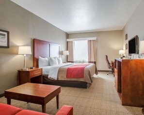 A hotel room with a bed, bedside tables, a desk, a chair, a TV, and a window with curtains.