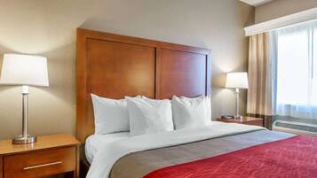 A hotel room with a large bed, two bedside tables, a wooden headboard, and a window with curtains.