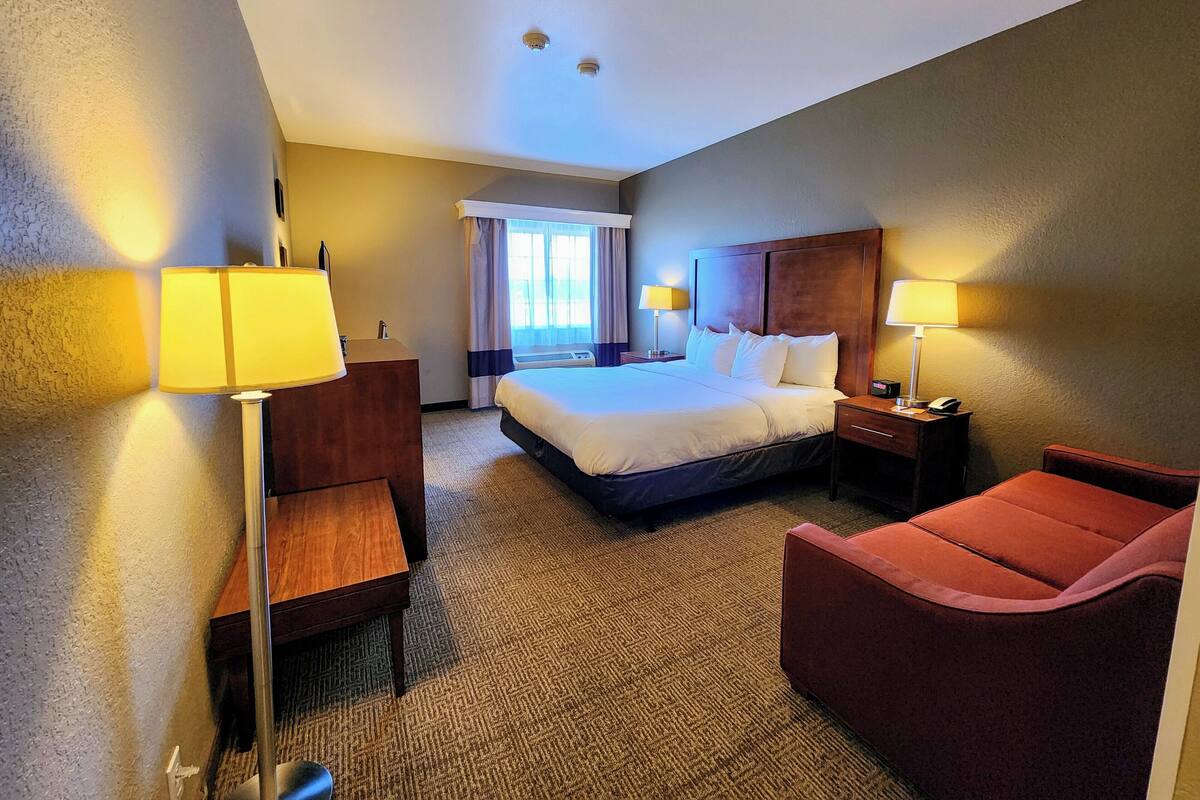 A hotel room with a large bed, two bedside tables with lamps, a desk, a chair, and a window with curtains.