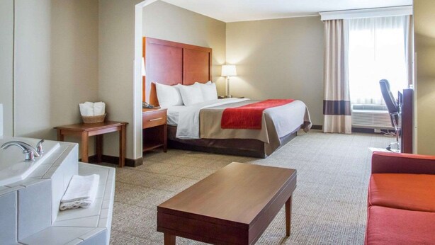 A hotel room with a bed, a desk, a chair, a sofa, a bathroom with a sink and mirror, and a window with curtains. - Comfort Inn Bolivar (Bolivar)