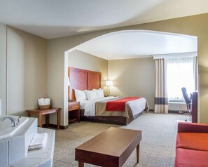 A hotel room with a bed, a desk, a chair, a sofa, a bathroom with a sink and mirror, and a window with curtains.