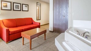 A hotel room with a red sofa, a wooden coffee table, a large mirror, and a white bathtub with a towel. - Comfort Inn Bolivar (Bolivar)