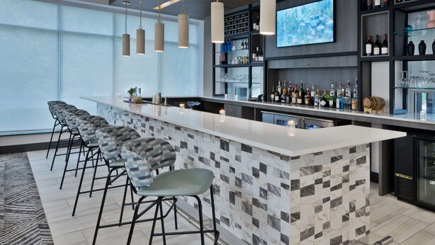 A modern bar area with a marble-tiled bar counter, multiple bar stools, and a wine and liquor display.
