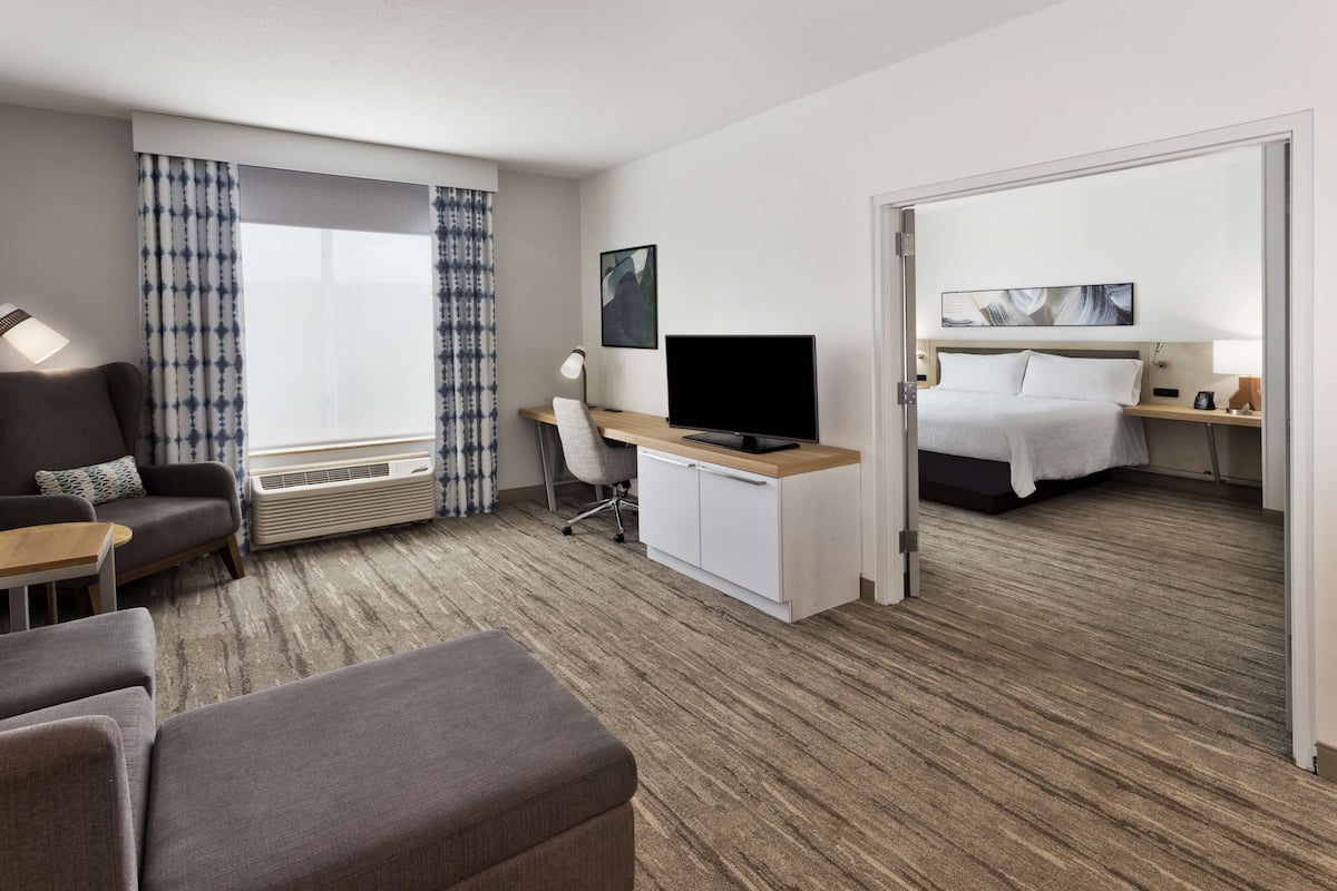 A hotel room with a sofa, a desk with a computer, a bed, and a large window with curtains.