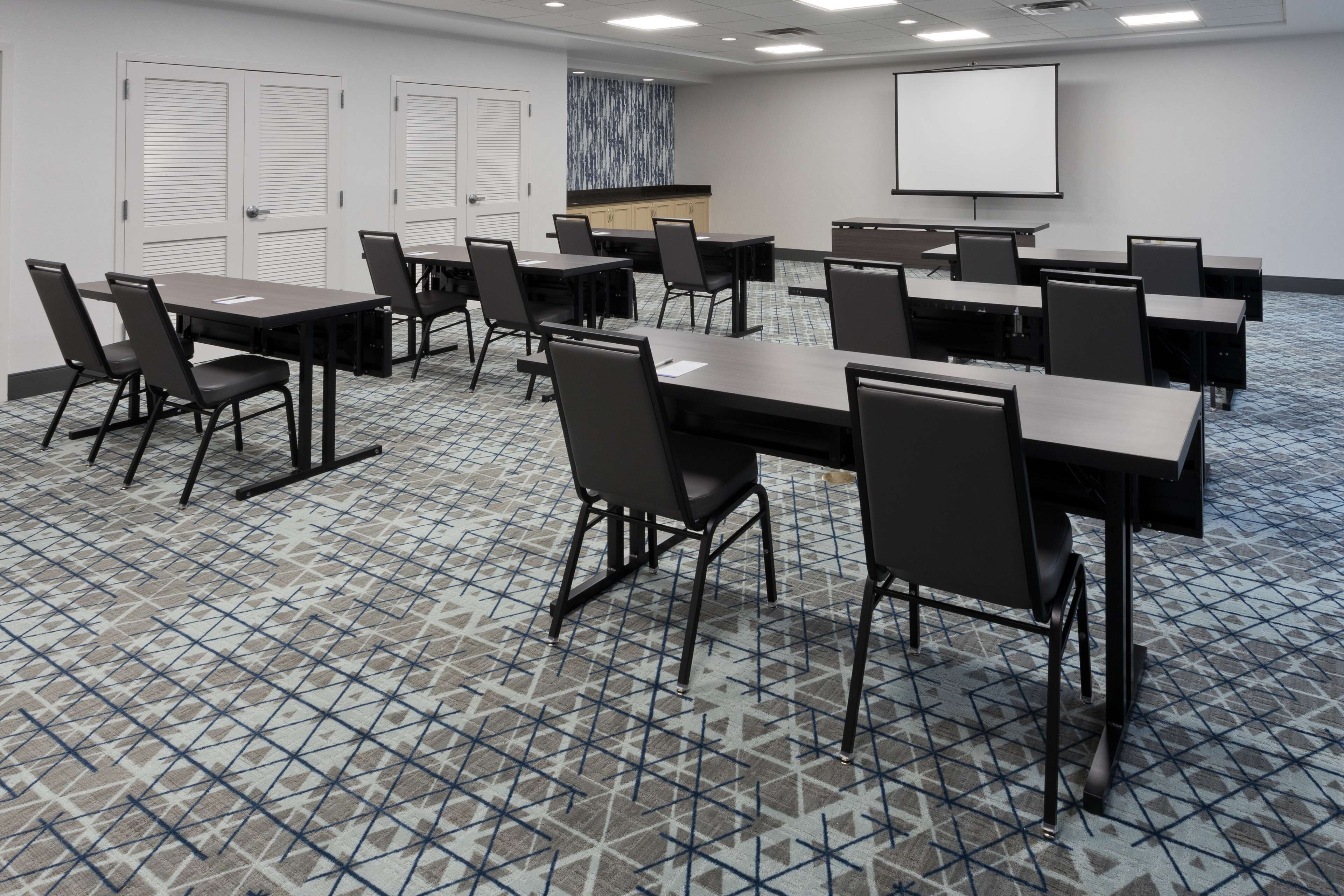 A conference room with multiple tables and chairs, a projector screen, and a patterned carpet.