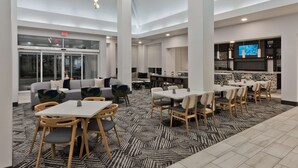A modern hotel lobby with a seating area, a bar, and a television screen.