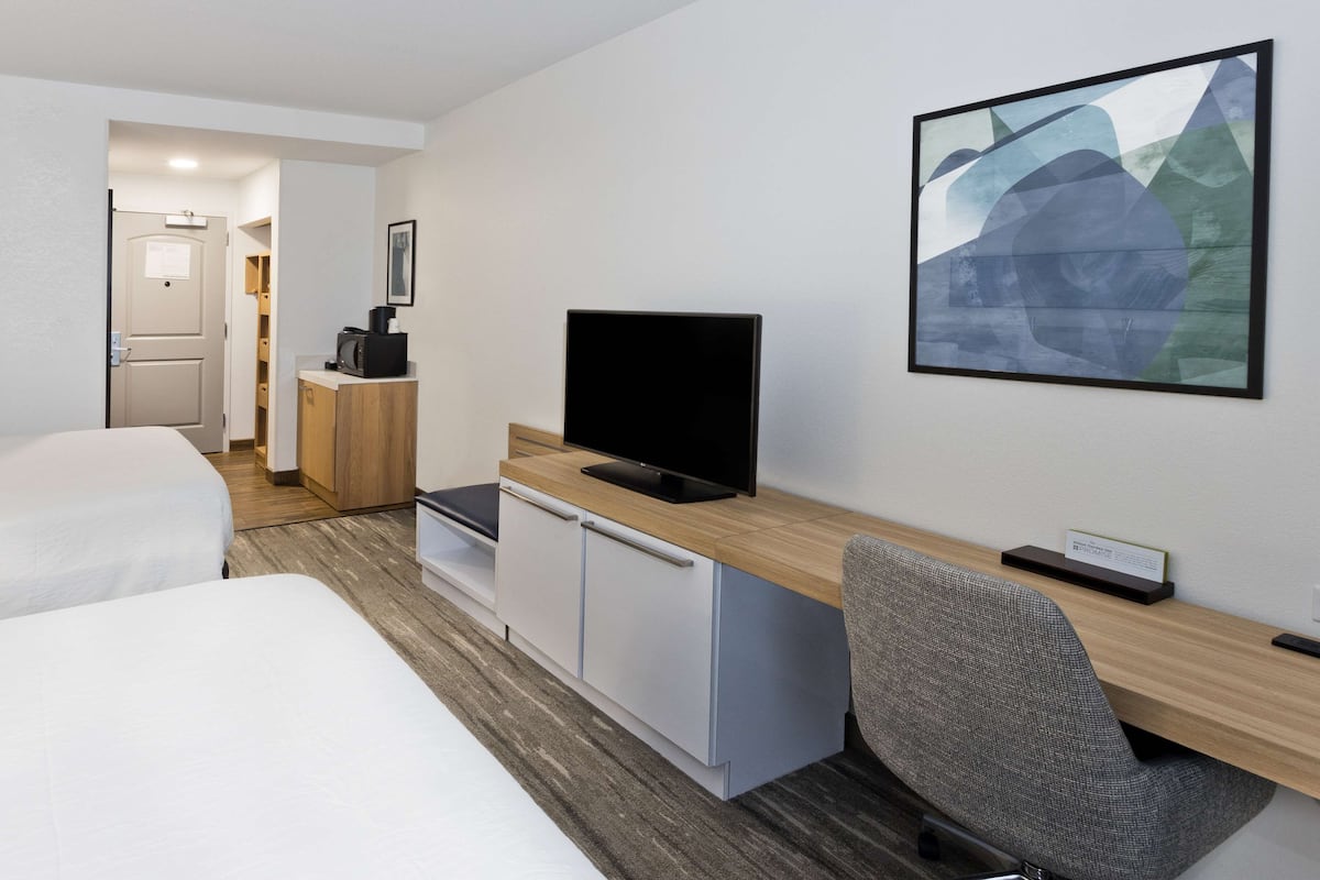 A hotel room with two beds, a desk with a TV, a chair, and a small cabinet.