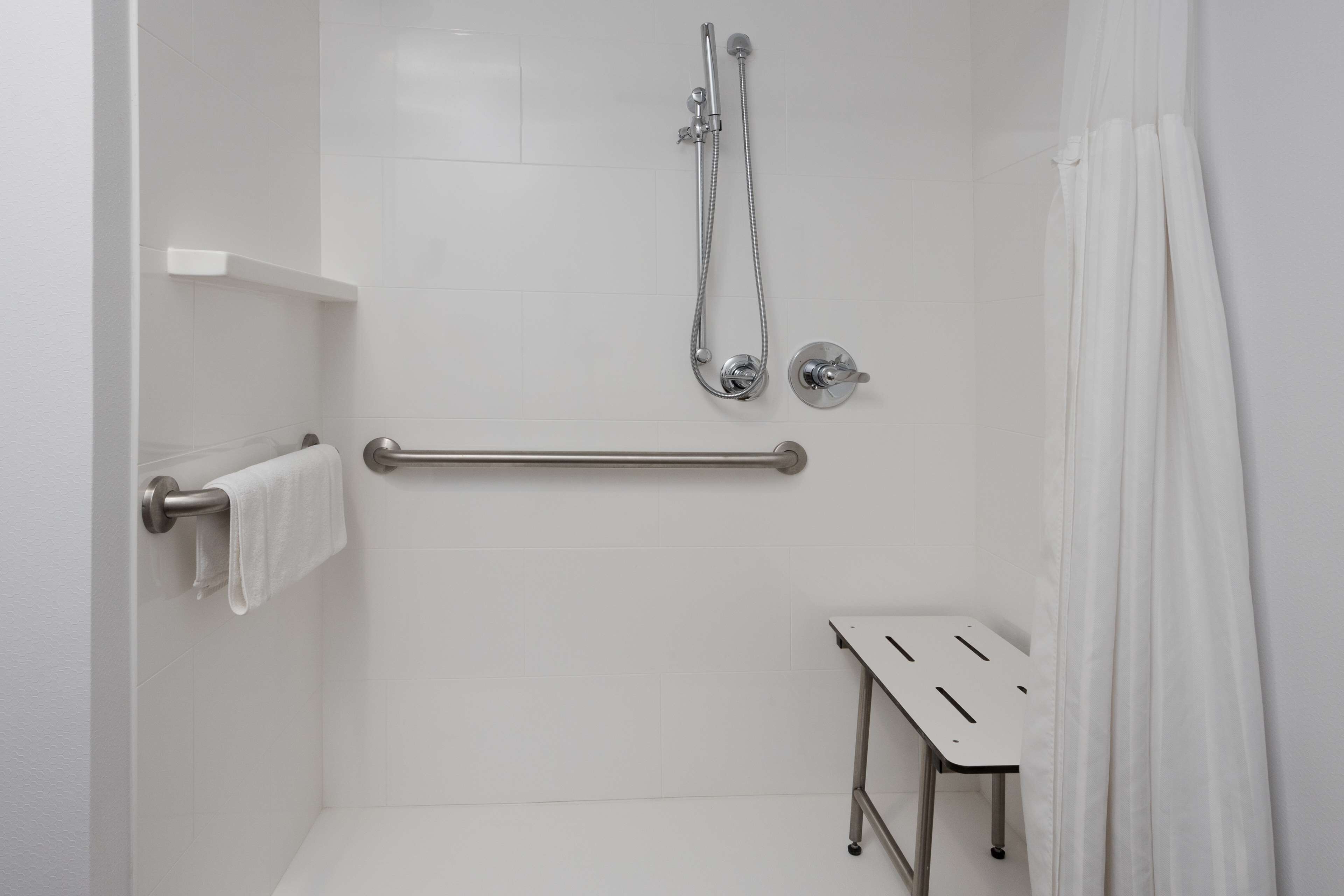 A modern bathroom with a shower, grab bar, and a small table.