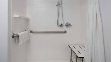 A modern bathroom with a shower, grab bar, and a small table.