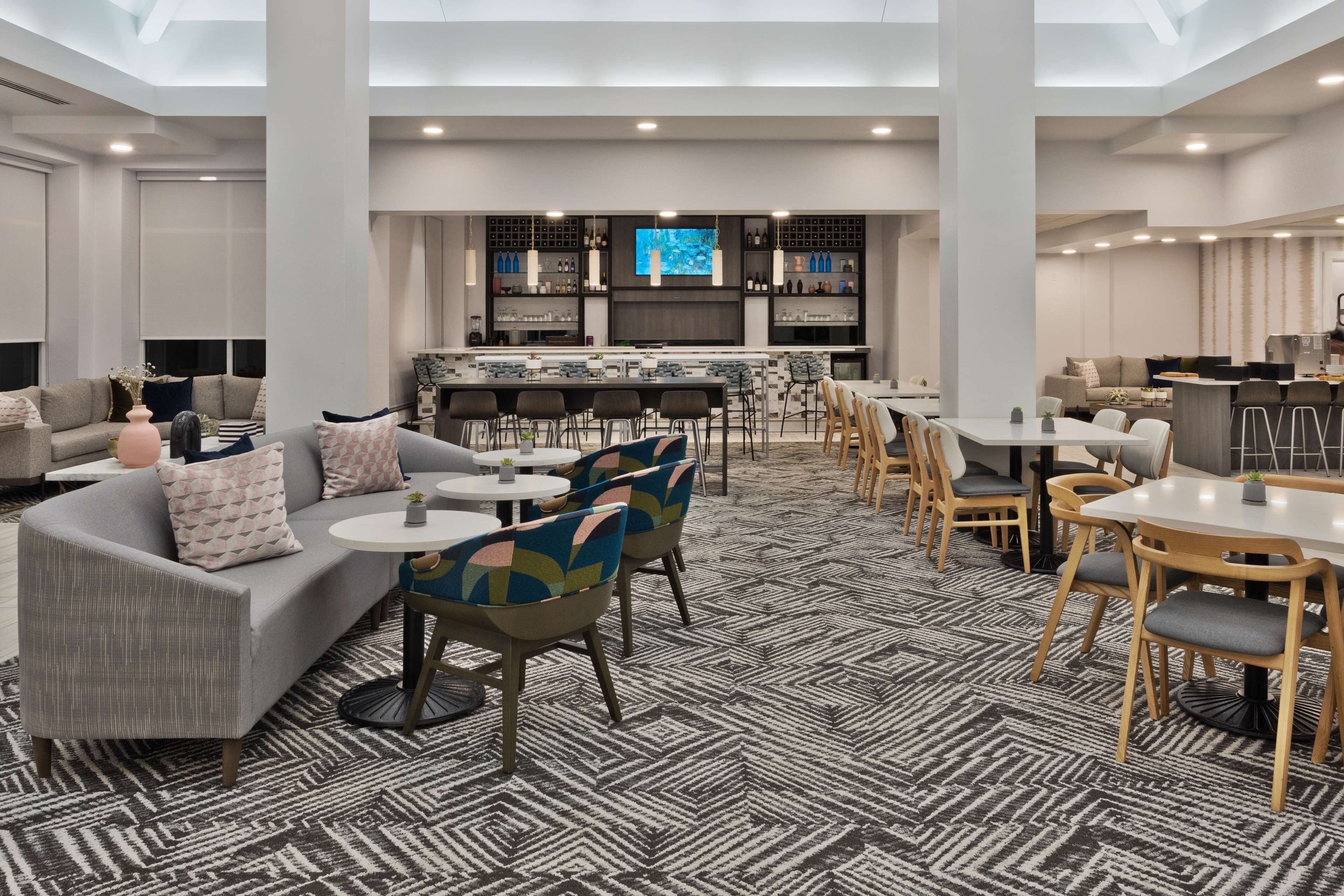 A modern hotel lobby with a bar area, seating arrangements, and a patterned carpet.