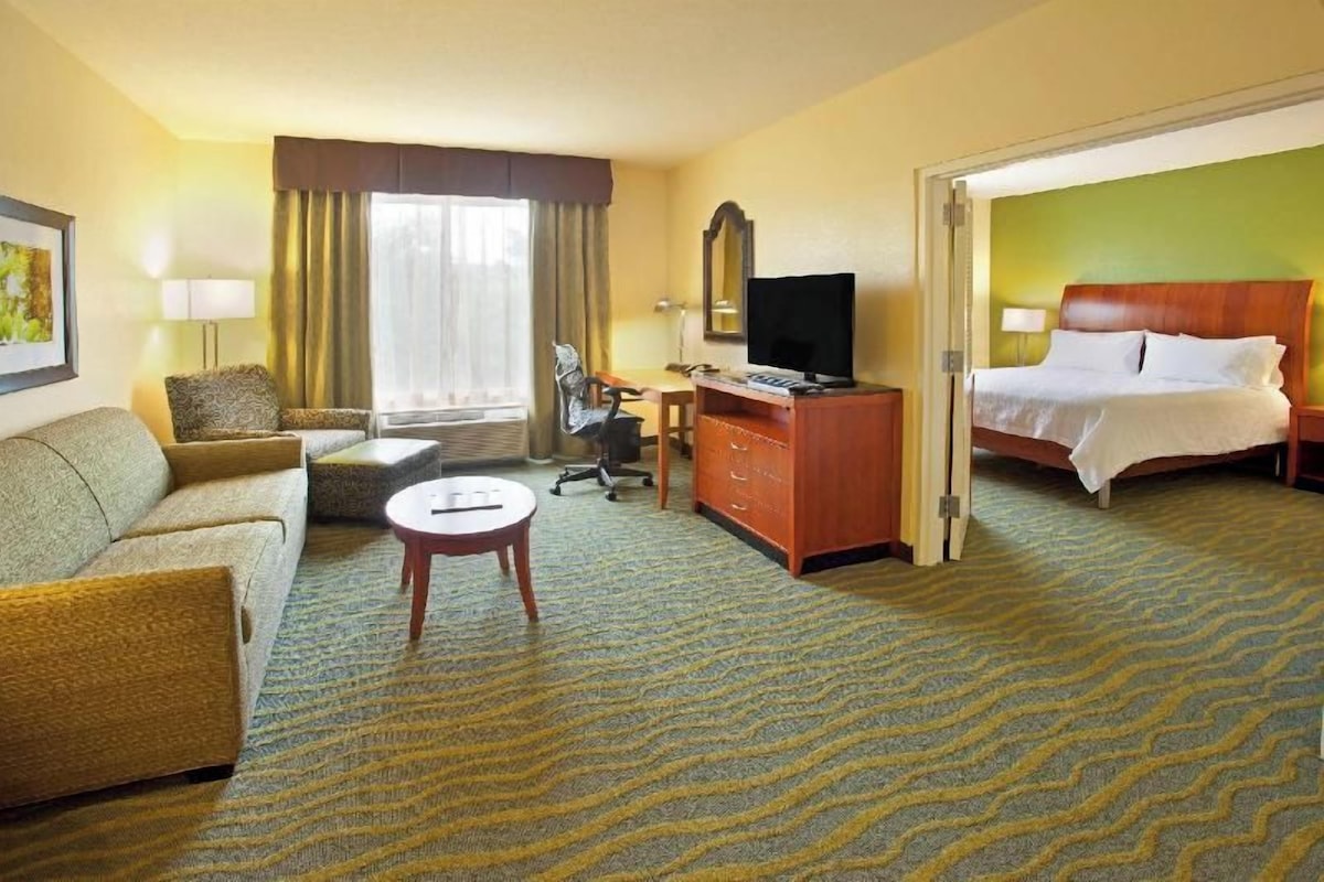 A hotel room with a bed, a sofa, a desk, a television, and a window with curtains.