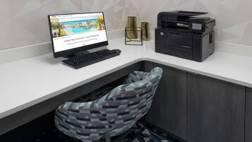 Uma secretária moderna com um computador, uma impressora e uma cadeira estampada.