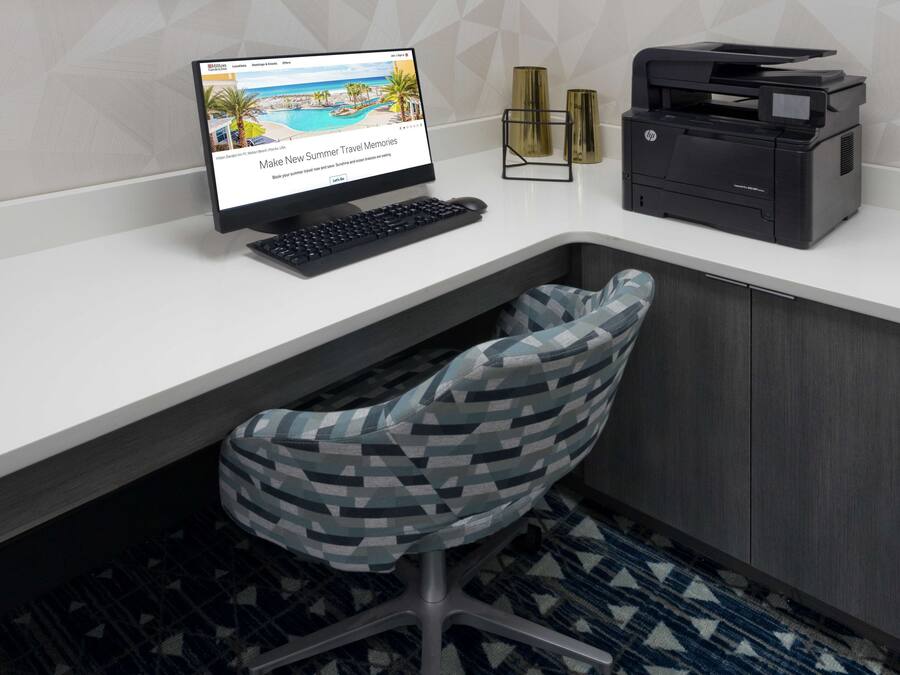Uma secretária moderna com um computador, uma impressora e uma cadeira estampada.