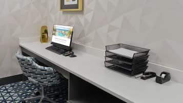 A modern office desk with a laptop, a chair, a printer, and a wall-mounted shelf.