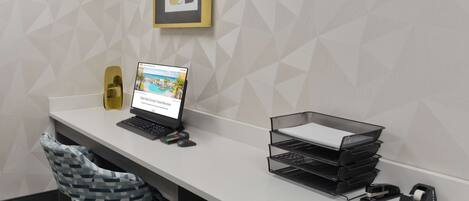 A modern office desk with a laptop, a chair, a printer, and a wall-mounted shelf.