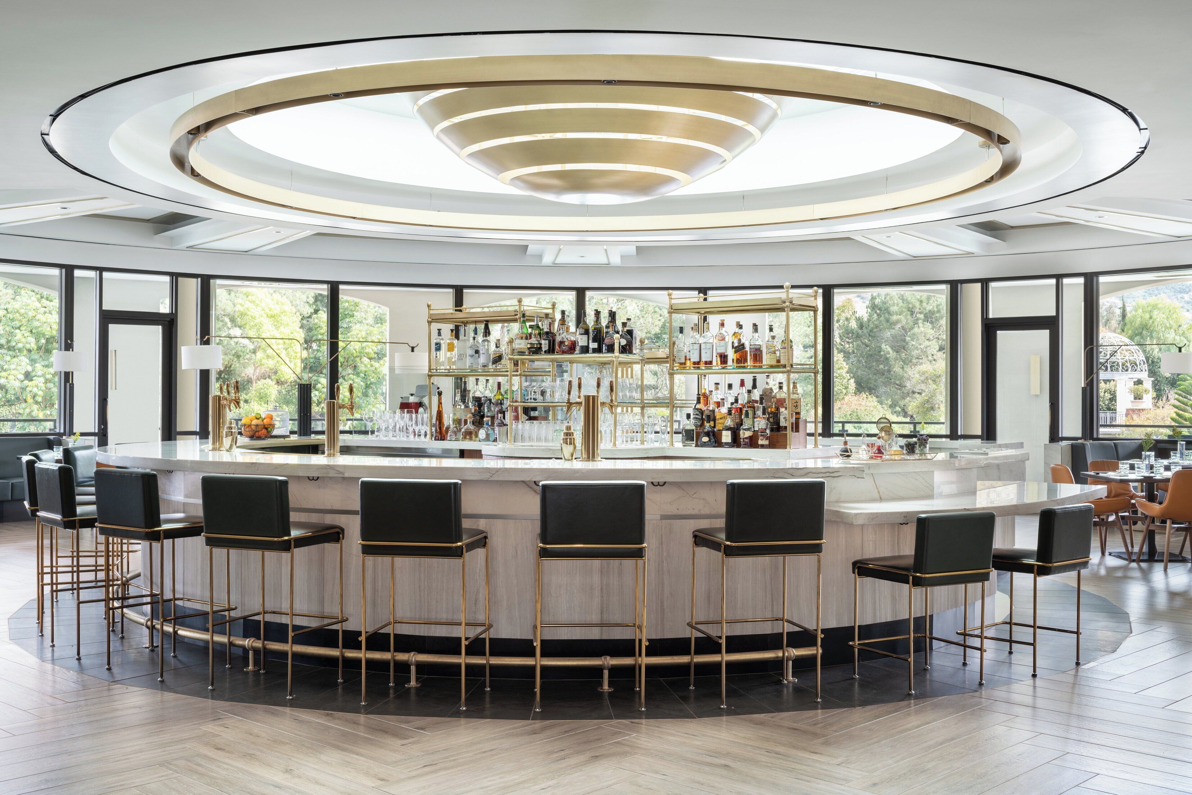 Un área de bar moderna con barra circular, varios taburetes y un estante bien surtido con diferentes botellas.