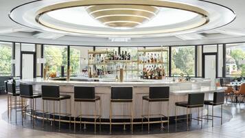 Un área de bar moderna con barra circular, varios taburetes y un estante bien surtido con diferentes botellas.