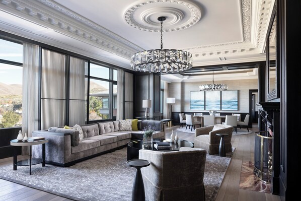 A spacious living room with a large sectional sofa, a round coffee table, and a chandelier. There is a fireplace and a large window offering a view of the outdoors. - Four Seasons Hotel Los Angeles at Westlake Village (Thousand Oaks)