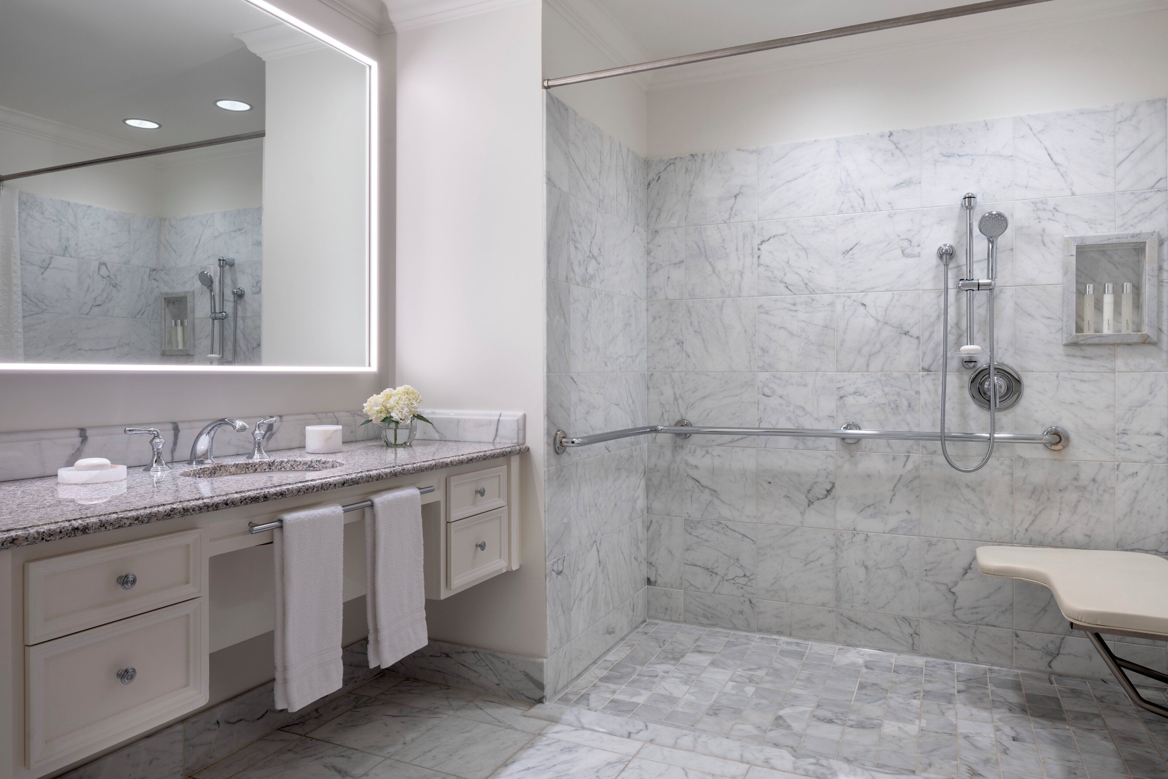 Une salle de bain moderne avec une douche en marbre, un meuble-lavabo avec un miroir et une barre d’appui pour faciliter l’accès.