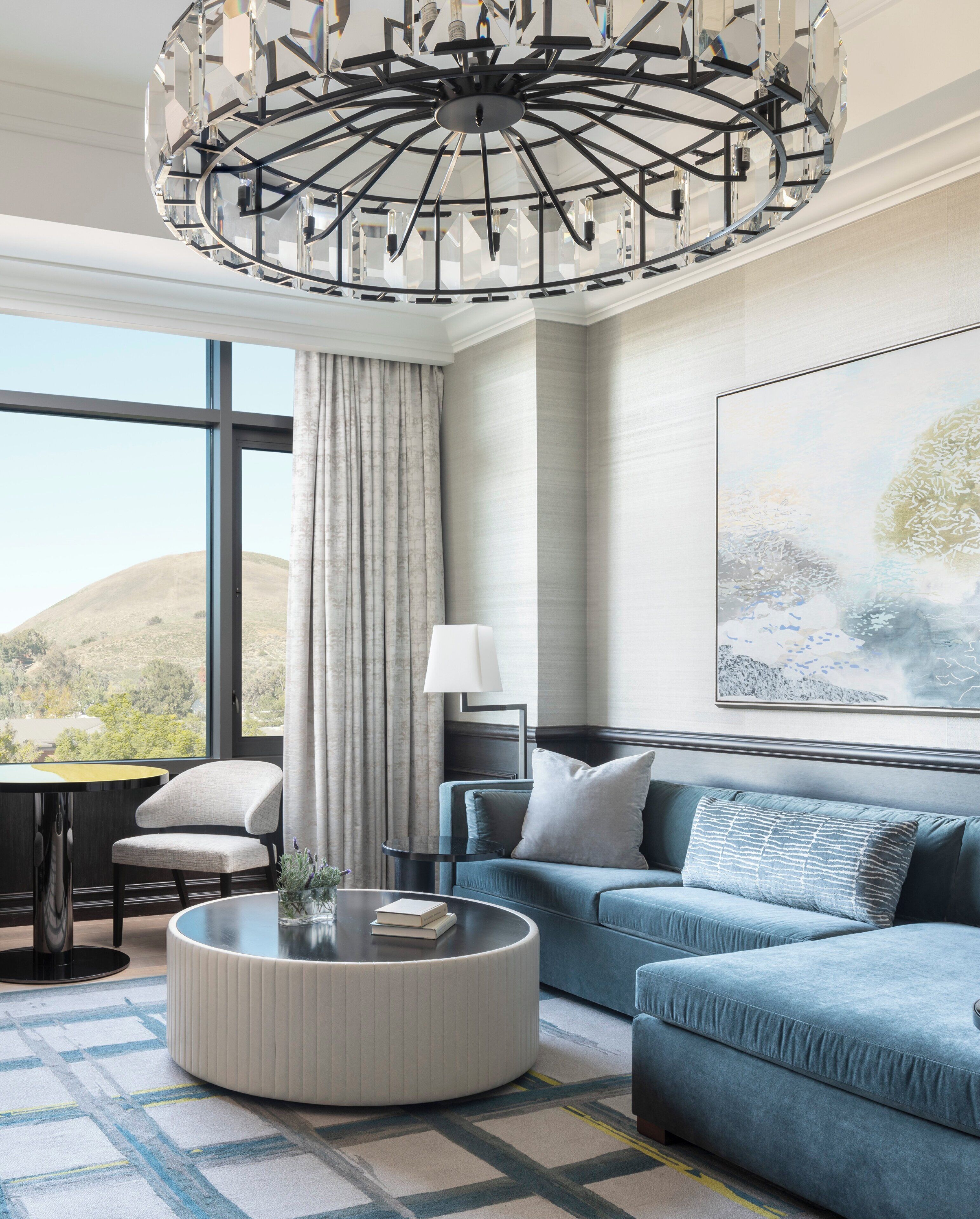 A modern living room with a blue sofa, a round coffee table, and a large abstract painting on the wall.