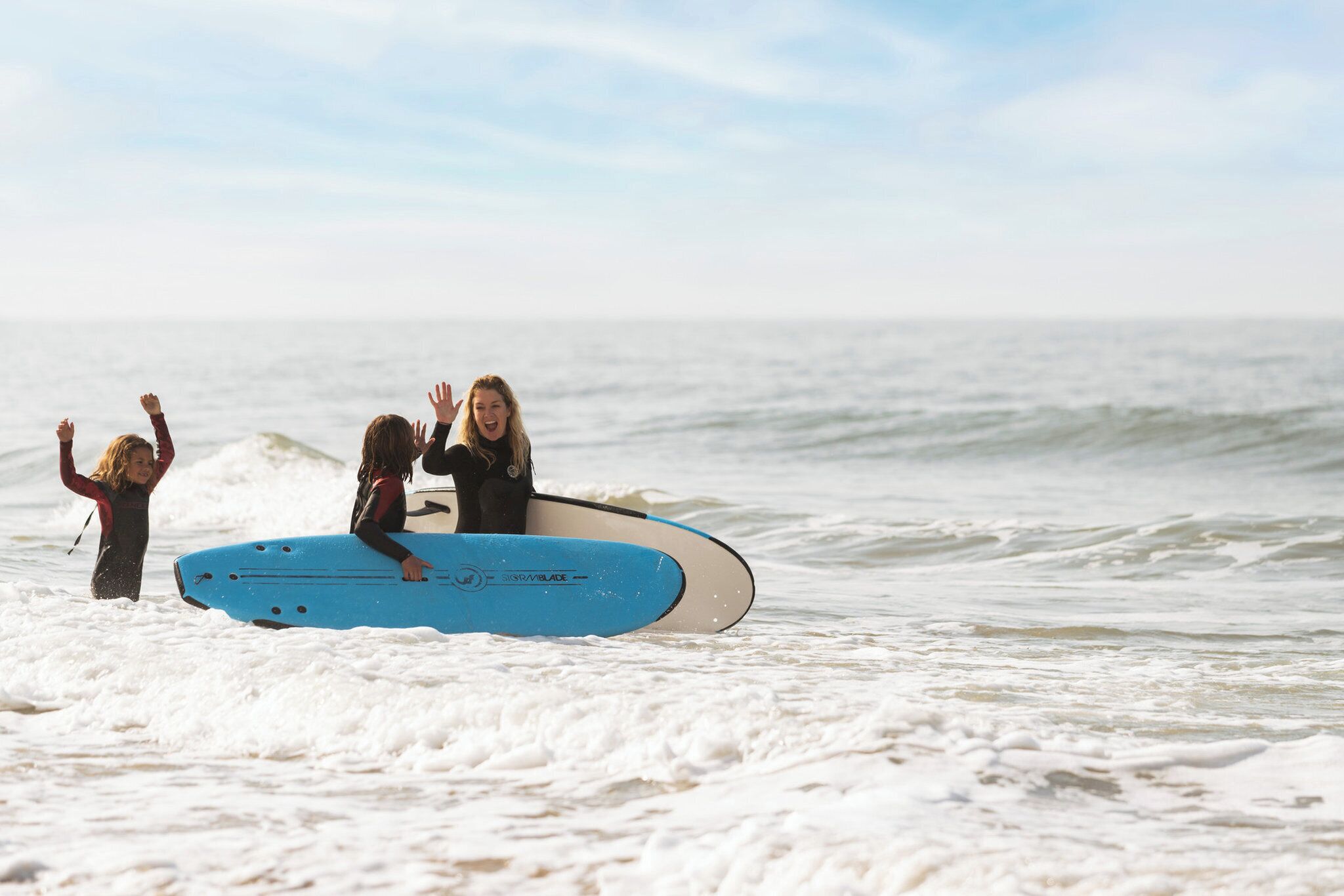 Duas pessoas com fatos de mergulho segurando uma prancha de surf azul na praia.