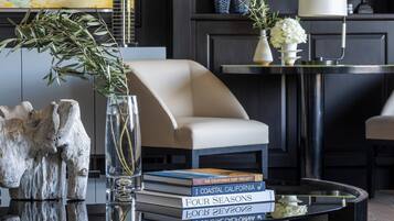 Un salon moderne avec un fauteuil en cuir, une table basse avec des livres, un vase avec une plante et une bibliothèque remplie de livres et d’objets décoratifs.