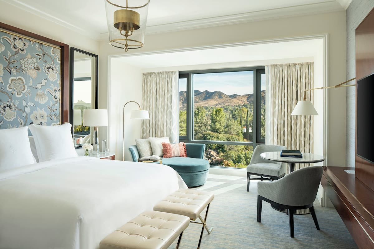 A hotel room with a large bed, a desk with a chair, a small round table, and a TV.
