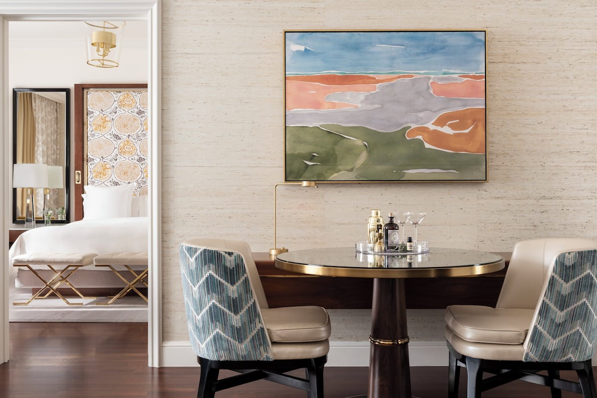 A modern dining area with a round table, two chairs, and a painting on the wall.