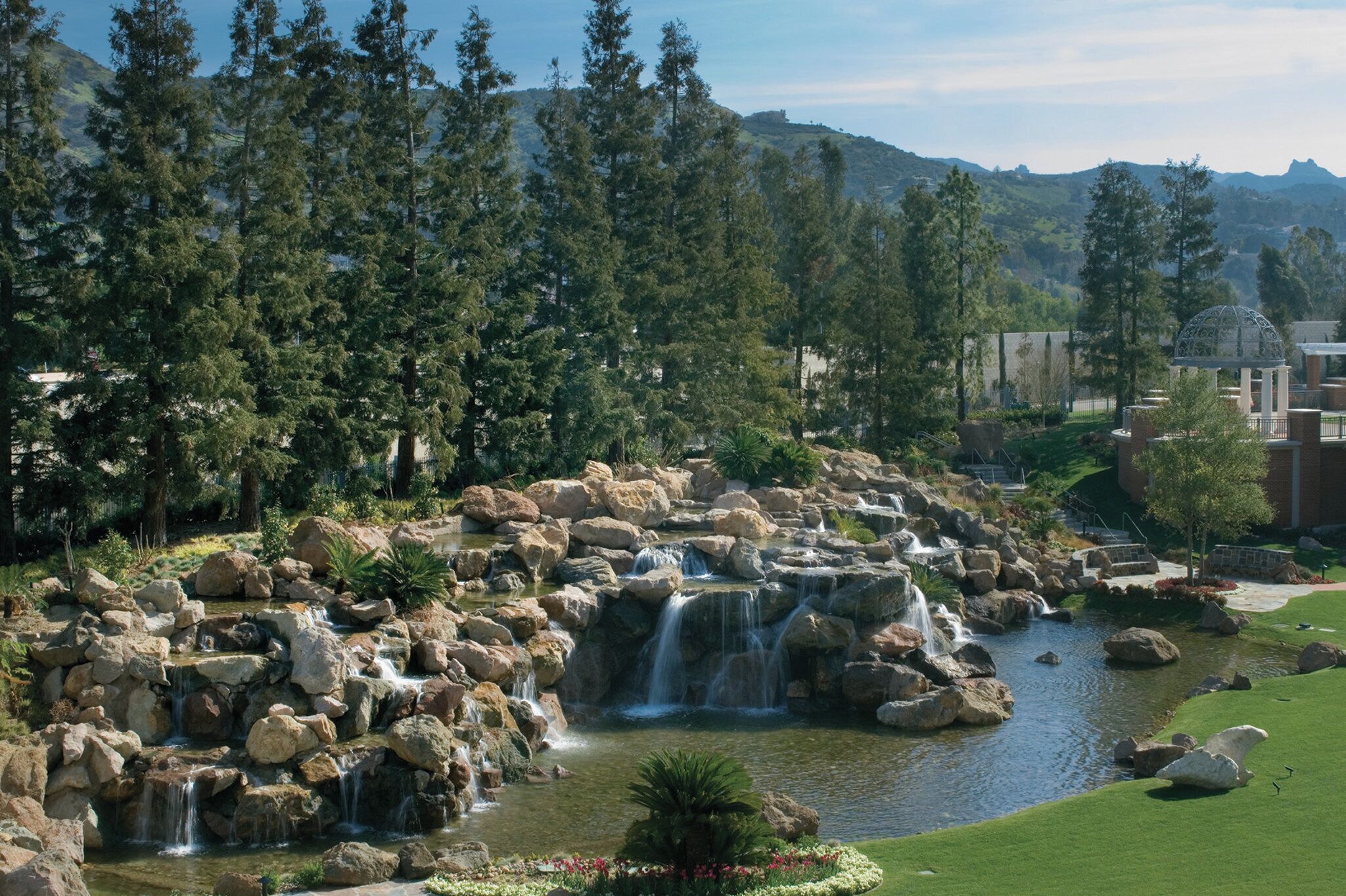 A landscaped garden with a pond, cascading waterfalls, and a gazebo.