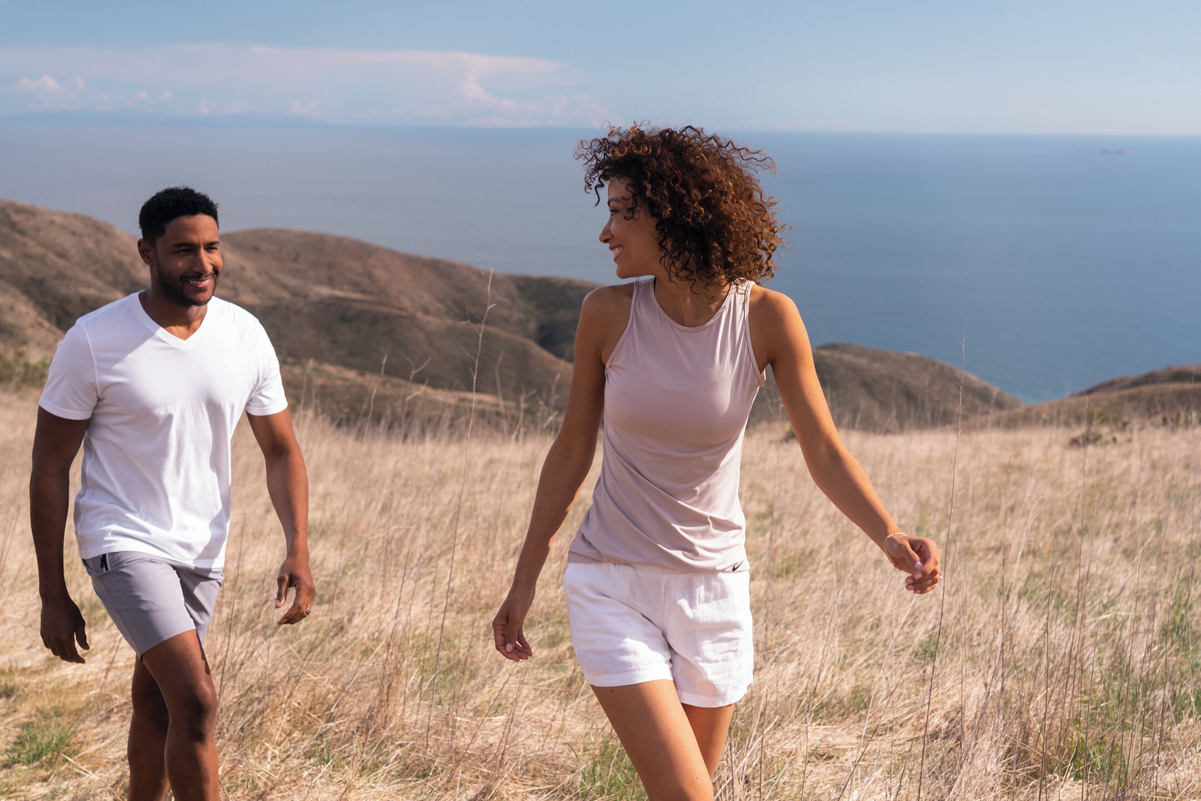 Two people walking on a grassy hill with a view of the ocean in the background.