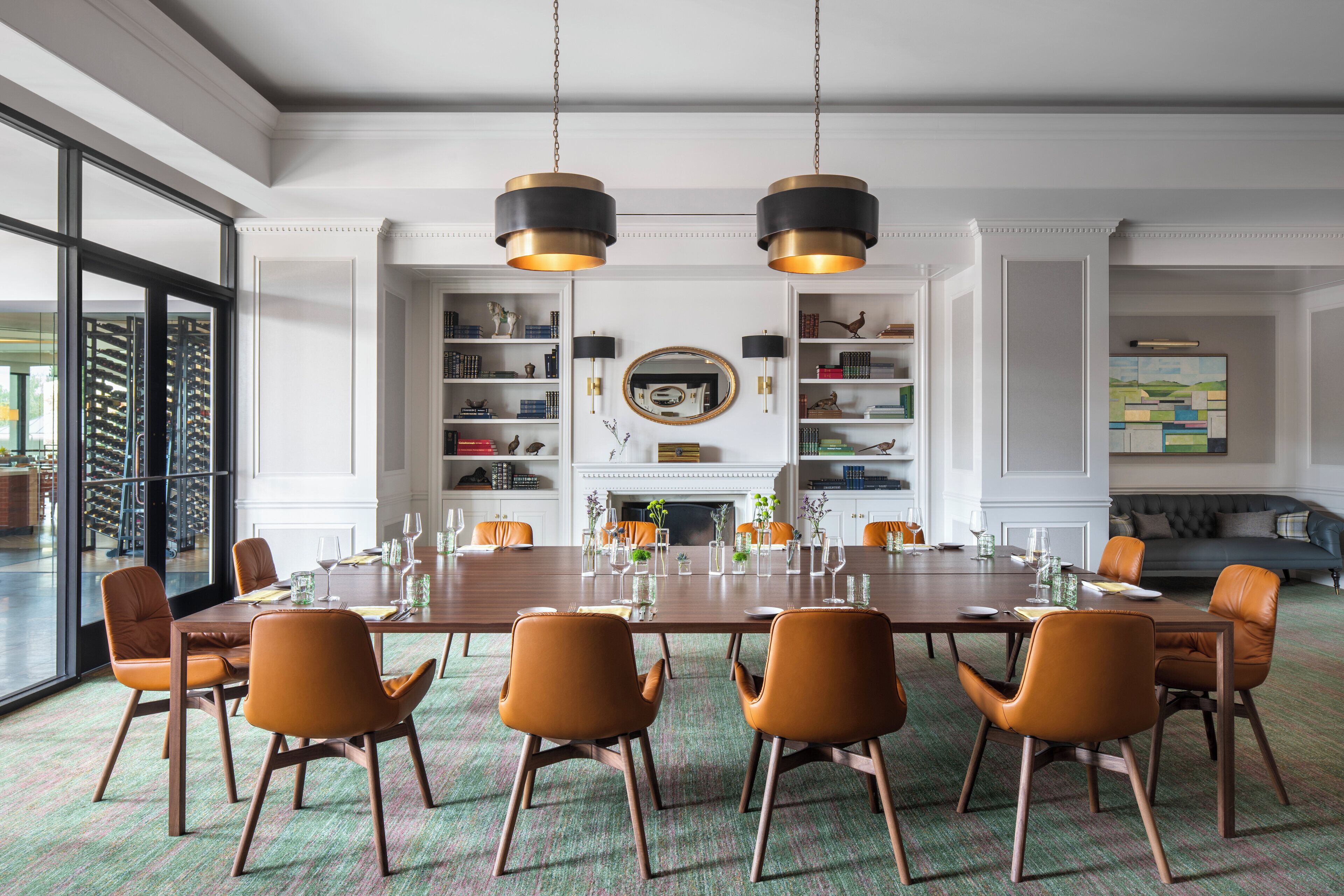 A spacious dining room with a large wooden table, six orange chairs, and two hanging pendant lights.