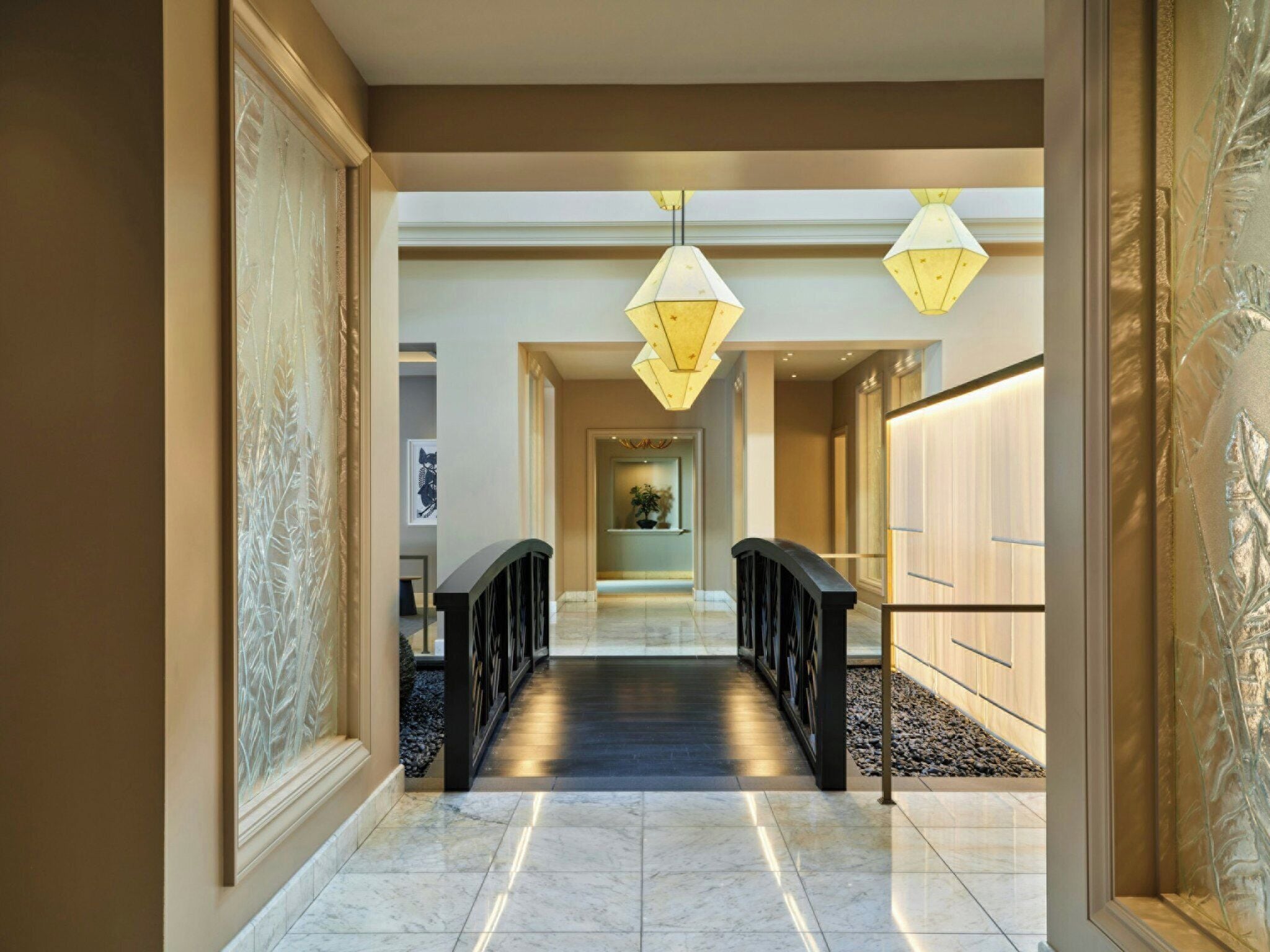 A hallway with a marble floor, black railings, and decorative wall panels.