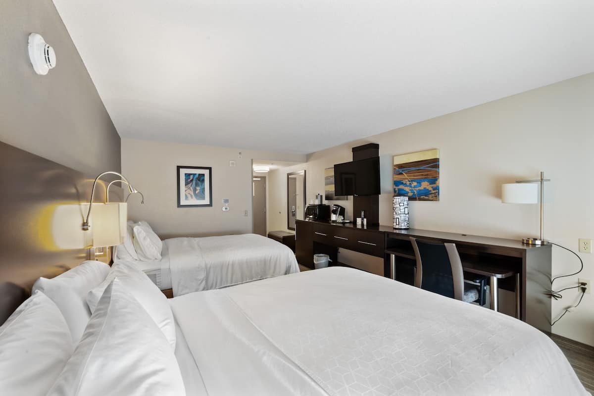 A hotel room with two beds, a desk, a chair, a TV, and a coffee maker.