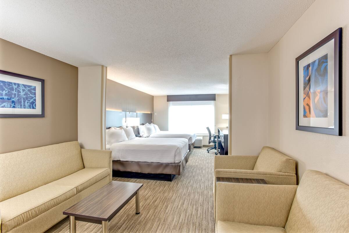 A hotel room with a sofa, a bed, a desk, and a chair. There are two beds in the room.
