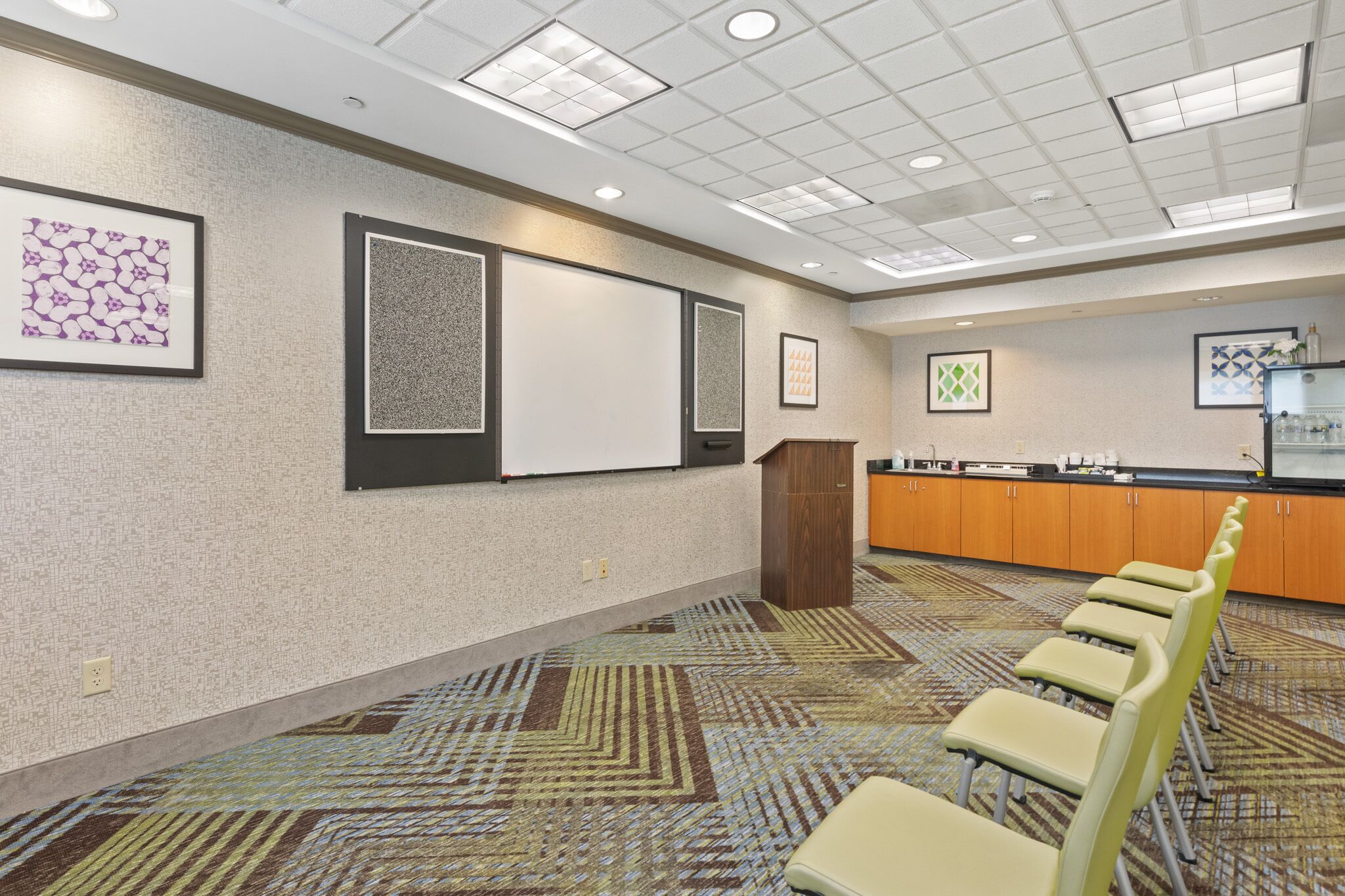 A conference room with a carpeted floor, a podium, a whiteboard, and framed artwork on the walls.
