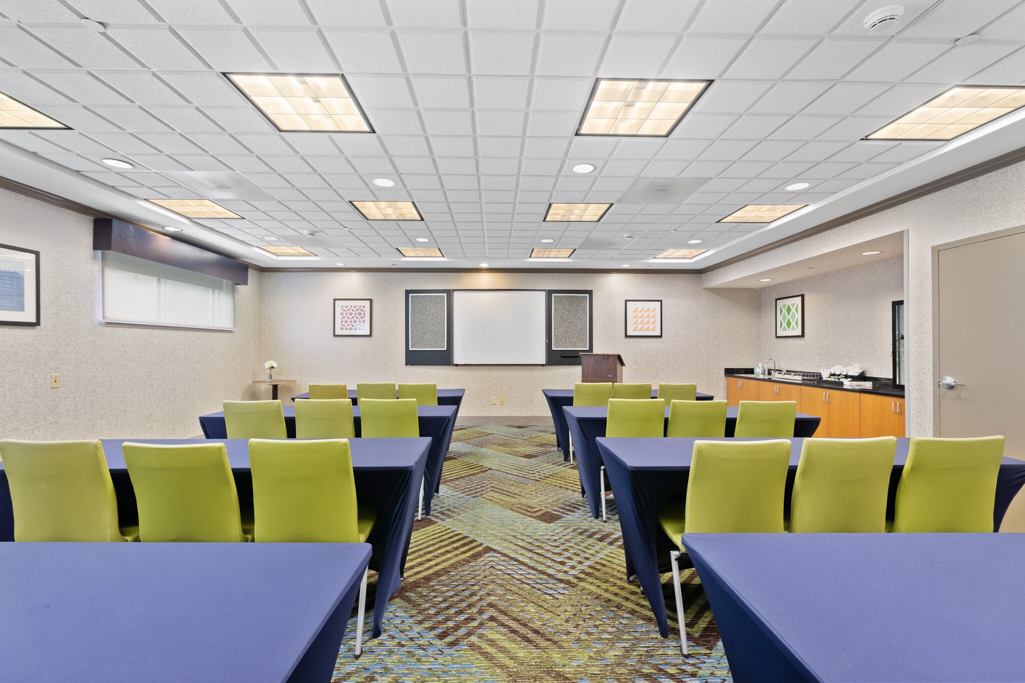 Une salle de conférence équipée de tables et de chaises, d’un pupitre et d’un écran de projection.