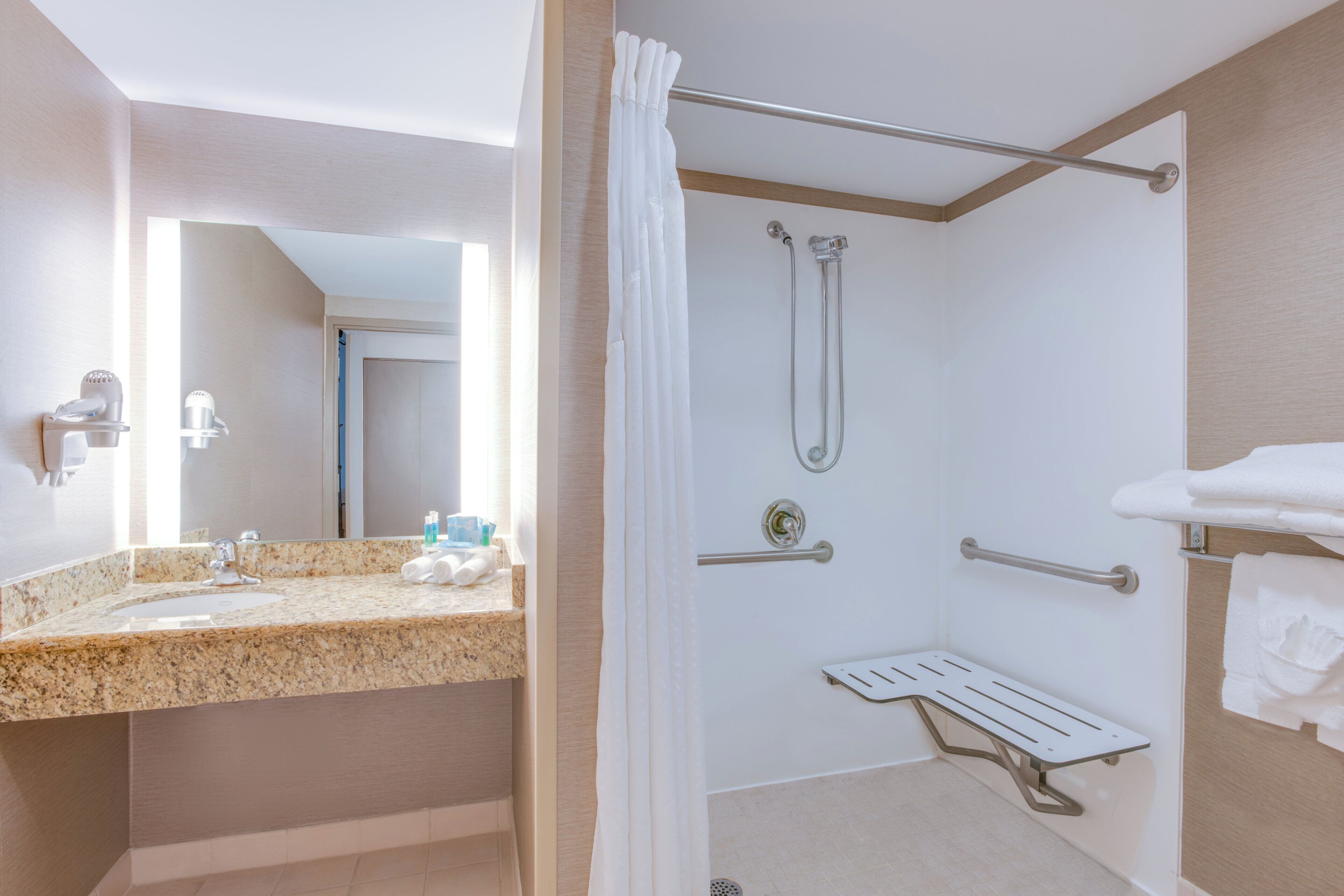 Un bagno d'hotel con lavabo in granito, doccia con soffione manuale e porta asciugamani.