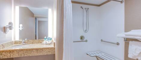 Un baño de hotel con lavamanos de encimera de granito, ducha con cabezal de ducha manual y toallero.