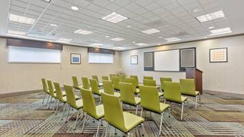 A conference room with rows of green chairs, a projector screen, and a podium.