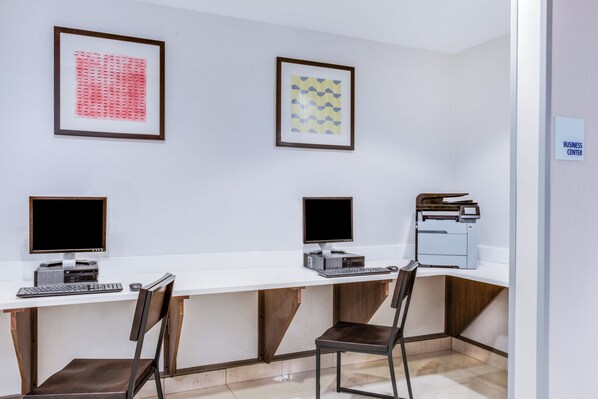 A modern office space with two desks, chairs, computers, and framed artwork on the wall.