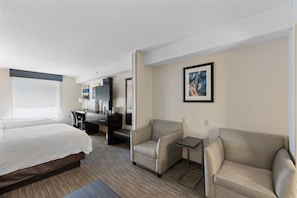 A hotel room with a bed, a desk, two armchairs, and a small table.