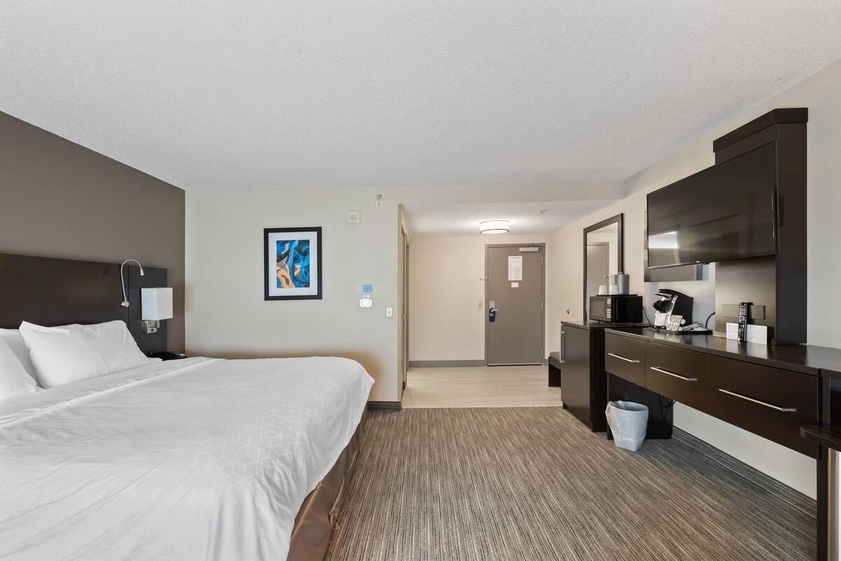 A hotel room with a large bed, a desk with a flat-screen TV, a microwave, and a coffee maker.