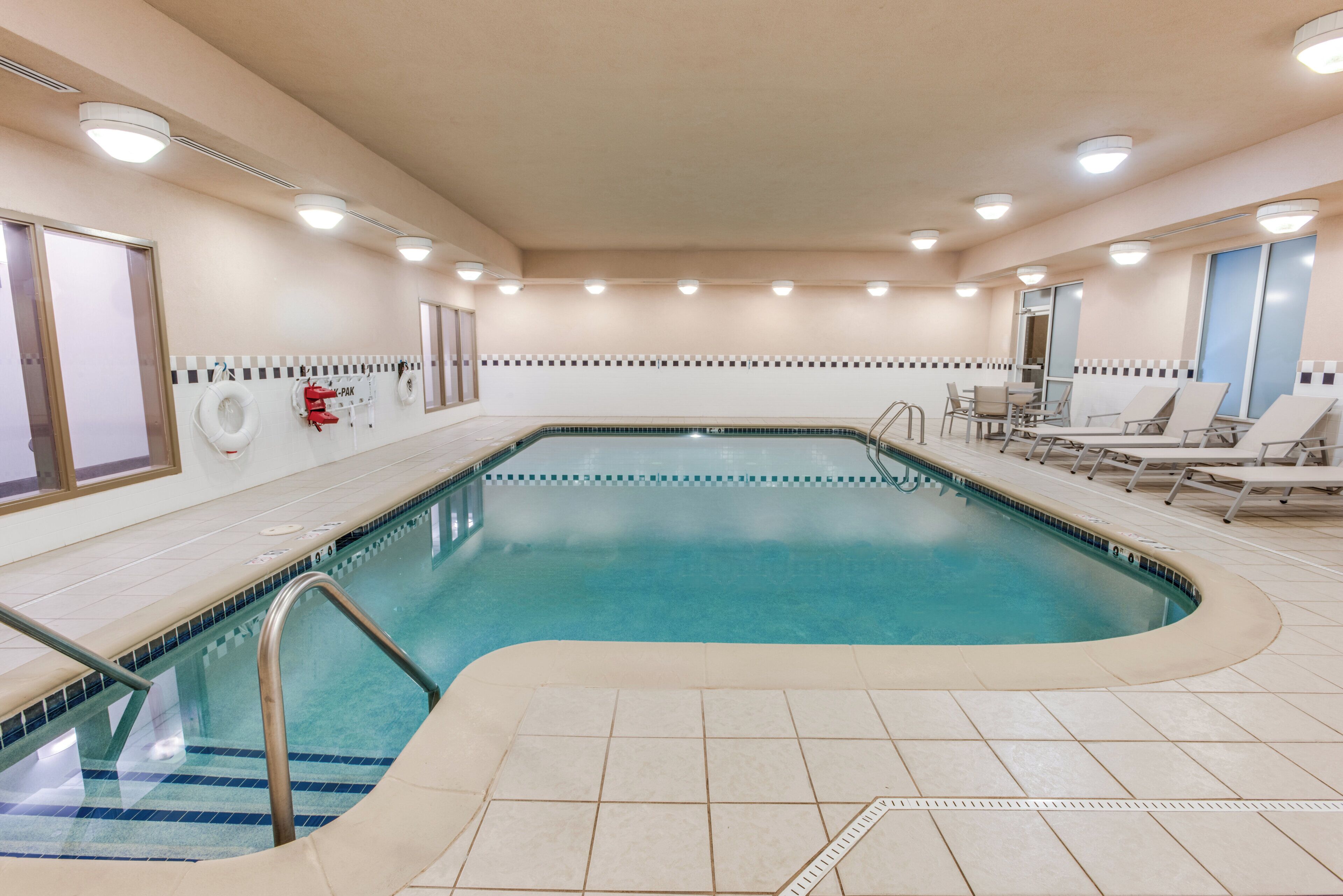 Una piscina con solárium empedrado, sillas de descanso y un puesto de socorrista.