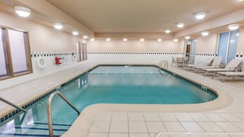 Una piscina con solárium empedrado, sillas de descanso y un puesto de socorrista.