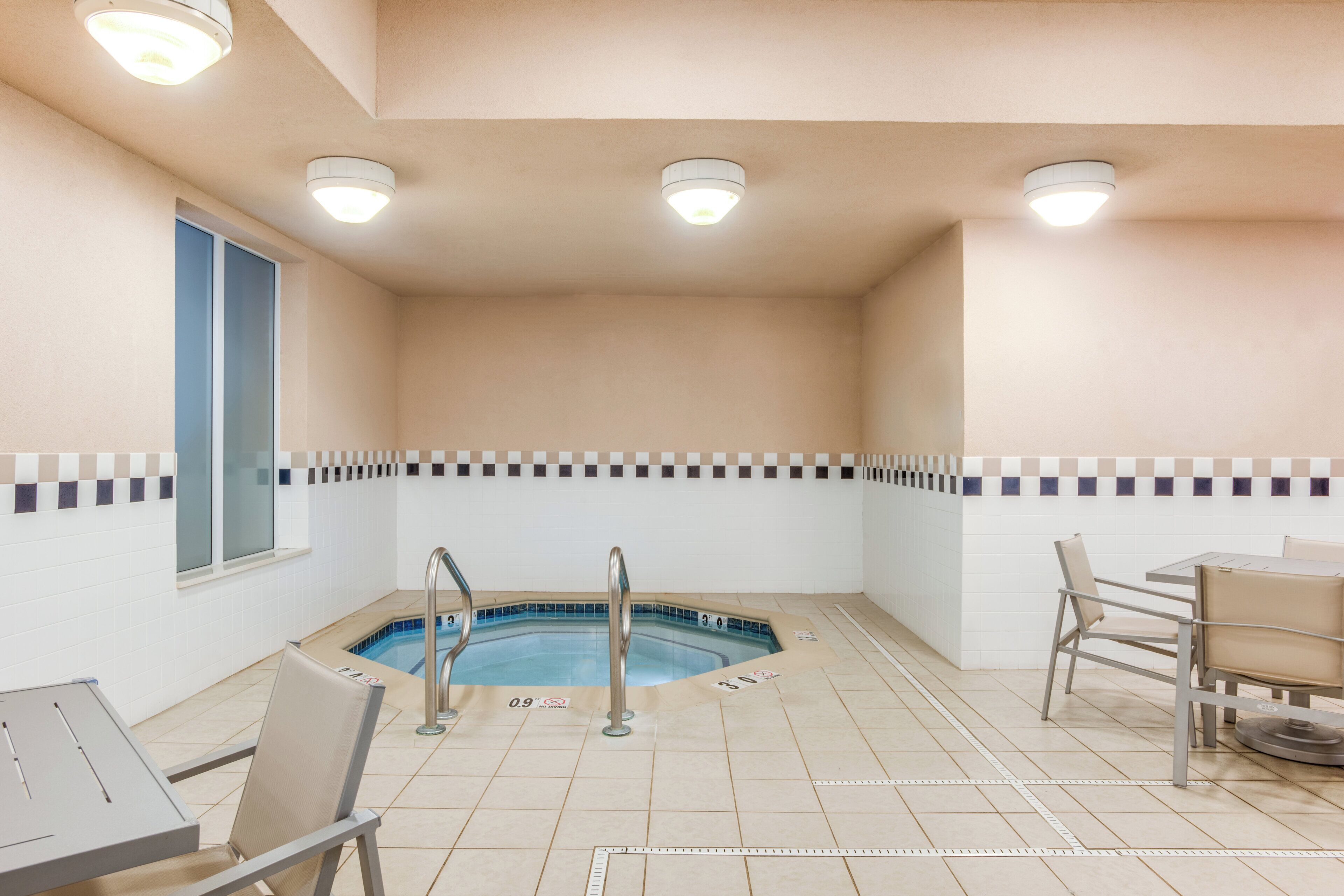 Un petit espace intérieur avec une piscine, un jacuzzi, une fenêtre et un coin salon avec des chaises.