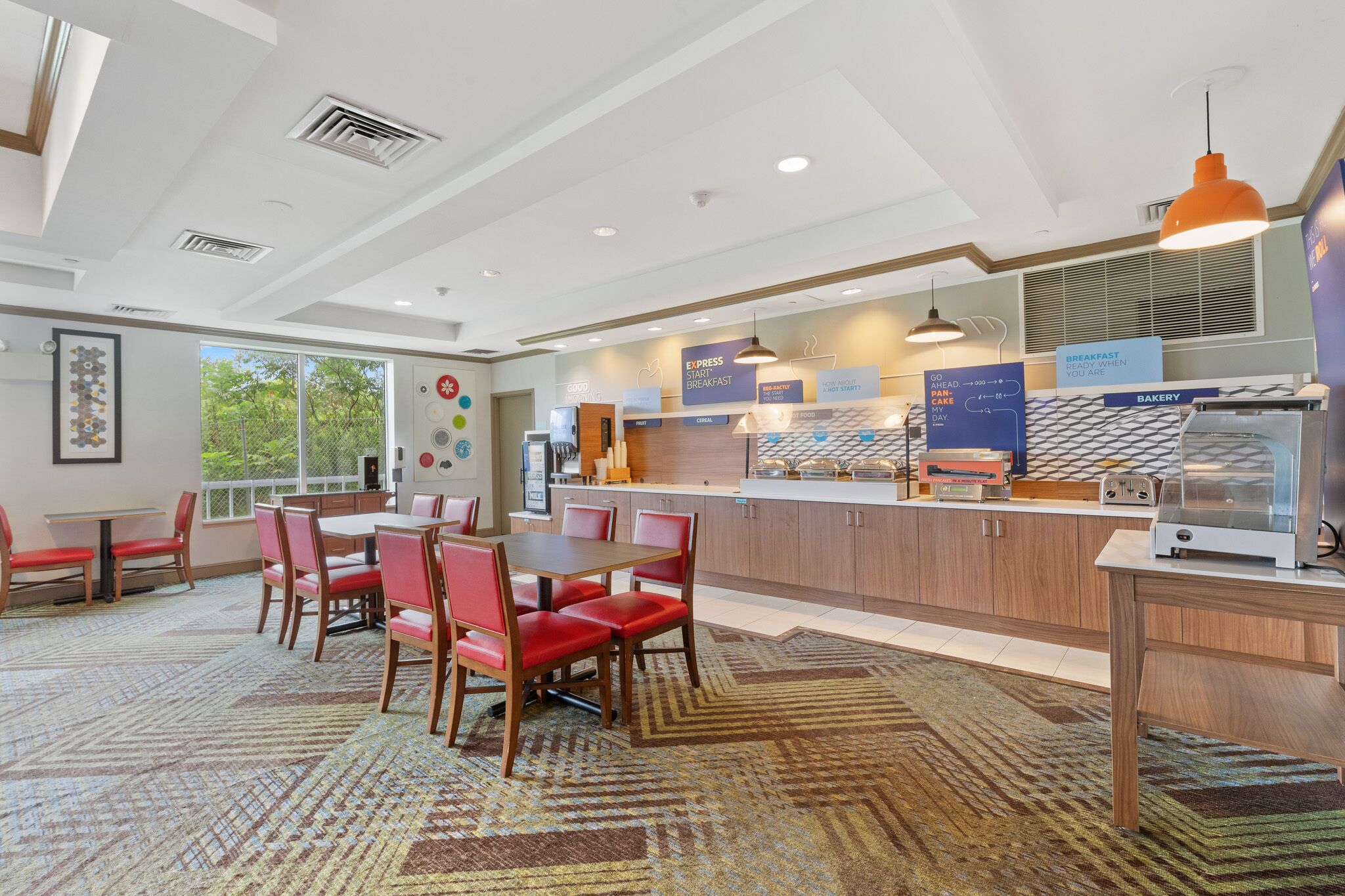 A modern dining area with a long counter, red chairs, and a patterned carpet.